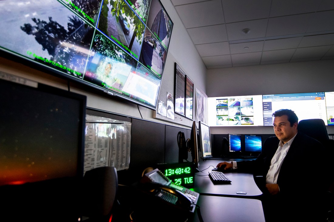A person monitors global campus safety from a control room filled with screens displaying maps and security camera feeds.