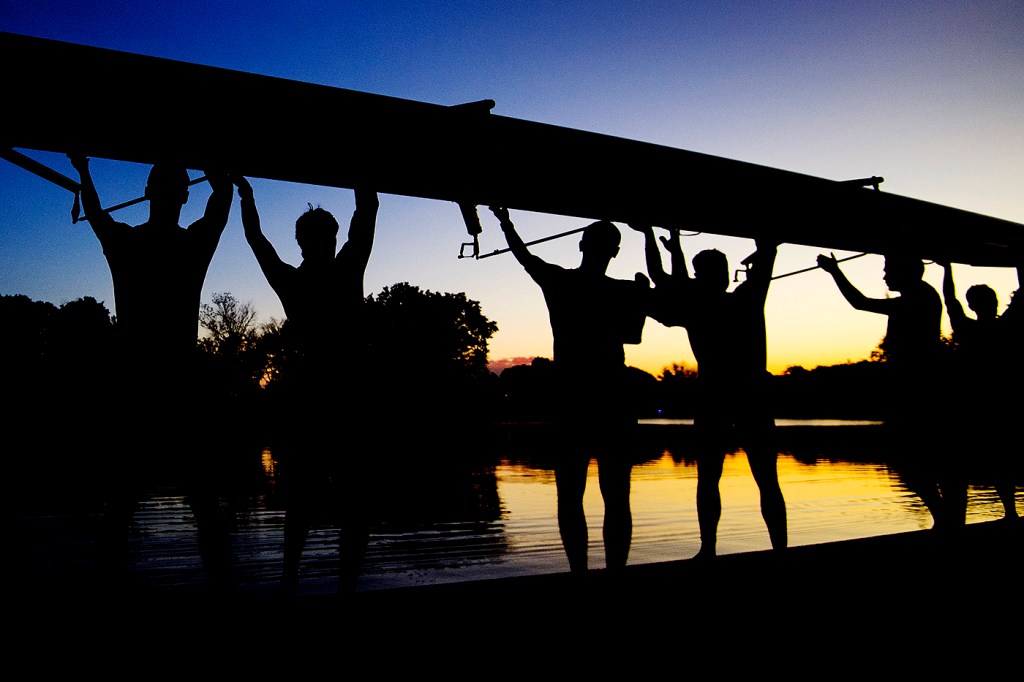 crew team hold boat next to the charles river