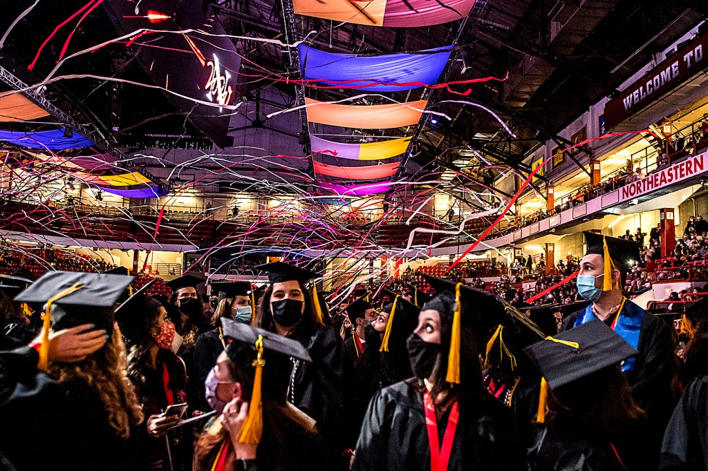 Graduates look up at streamers and brightly colored flags overhead