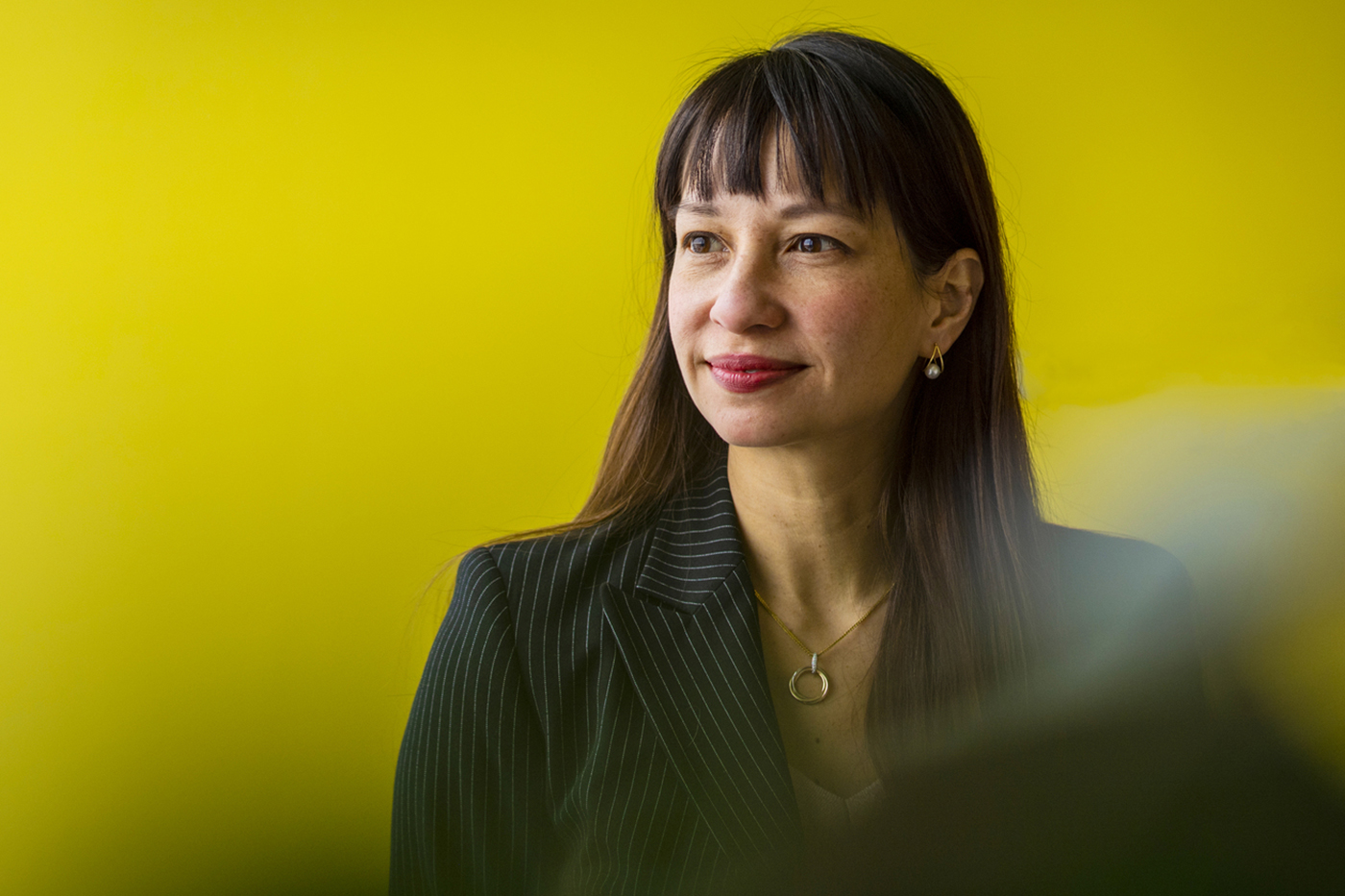 A portrait of Mai'a Cross, woman with dark hair on yellow background