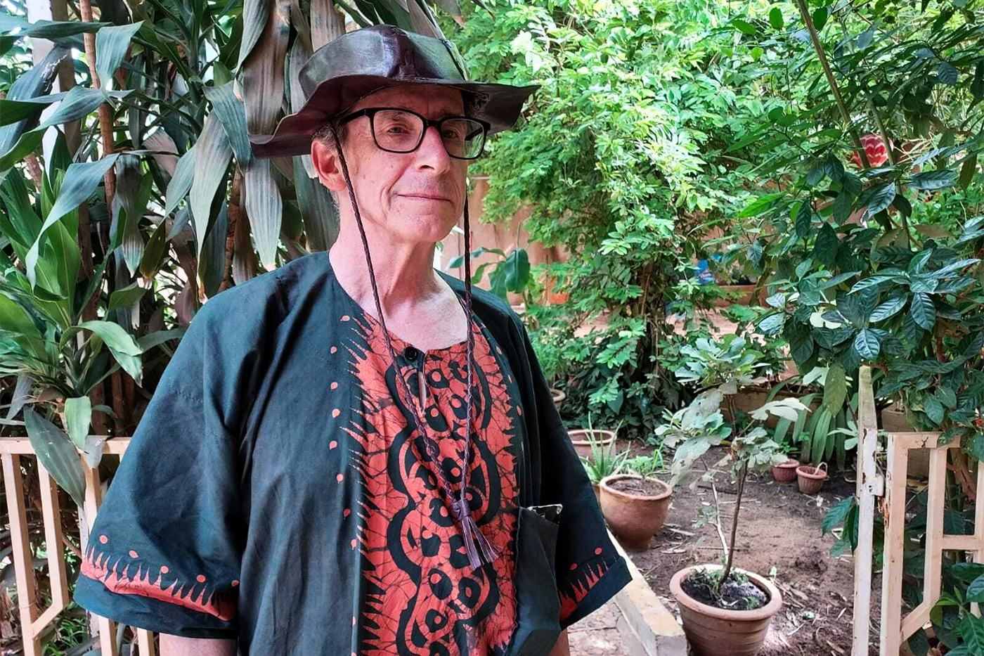 William Miles, outside surrounded by greenery and wearing a hat