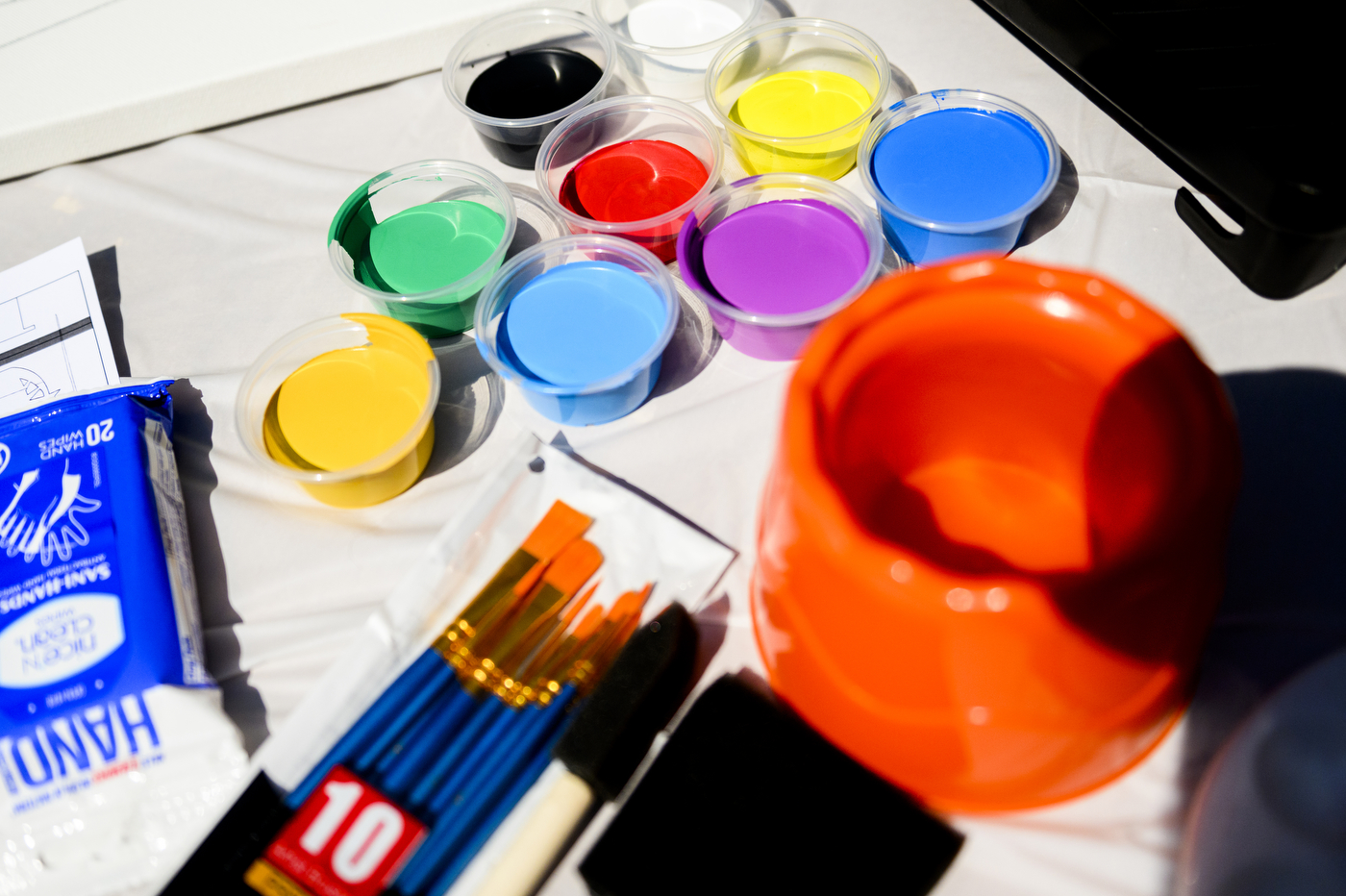 Paint, brushes, and an orange cup on a white table.