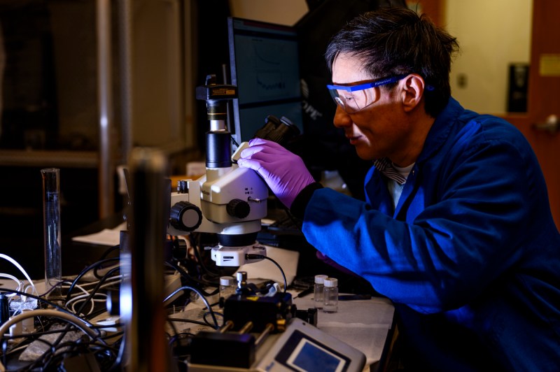 Hongwei Sun looking through a microscope in a lab.