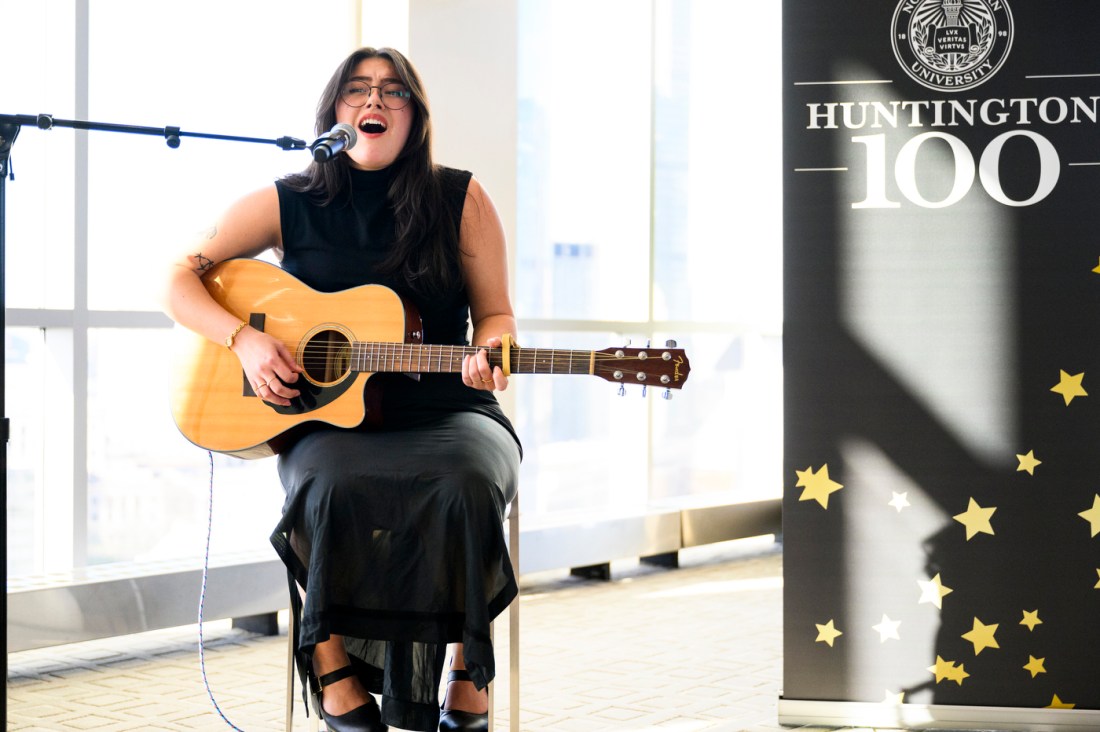 A person singing and playing guitar at the Huntington 100. 