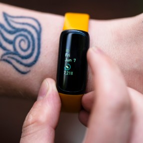 A hand checking a smart watch, which displays 7,218 steps.