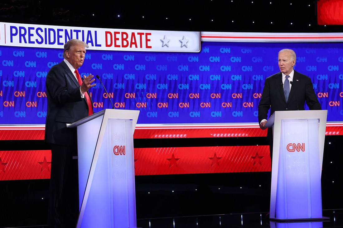 Former President Trump and President Biden stand in front of podiums in front of a bright blue, red background with red and blue text: 