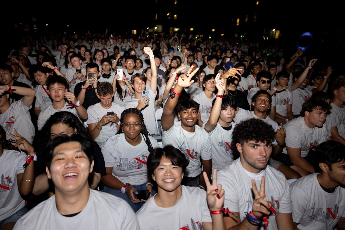 Students sitting in rows on the Oakland campus smile, wave, and hold up peace signs for the camera.