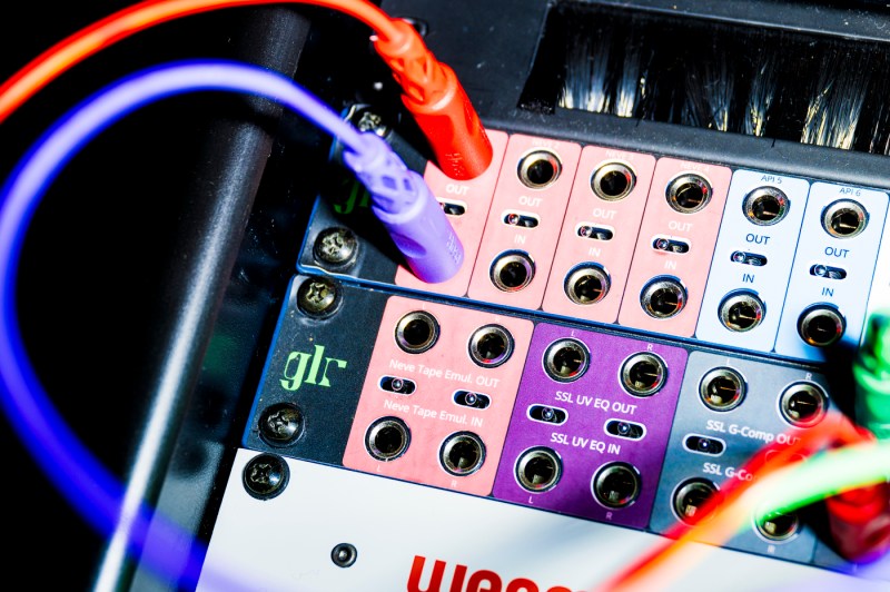 A purple and an orange cord both plugged into amplifiers on a mixing board.