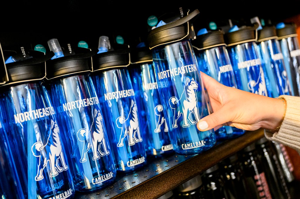 A person's hand picking up a Northeastern branded reusable water bottle from a shelf of them.