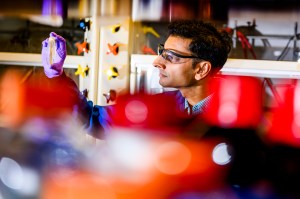 Neel Joshi, associate professor of chemistry and chemical biology, looks at a specimen in his lab, while wearing purple gloves and goggles.