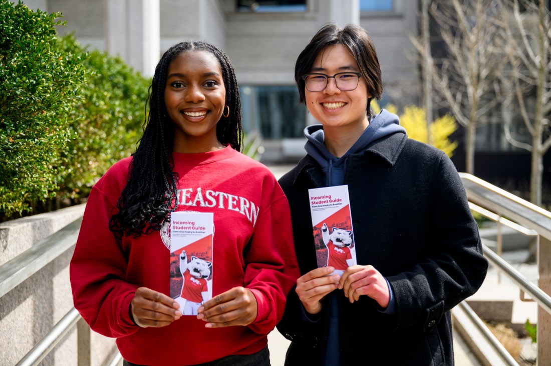 Two students holding pamphlets that say 'Incoming Student Guide' on them.