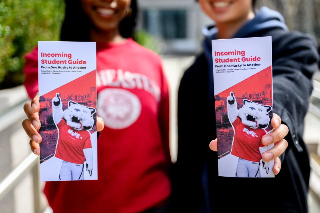 Two students holding pamphlets that say 'Incoming Student Guide' on them.