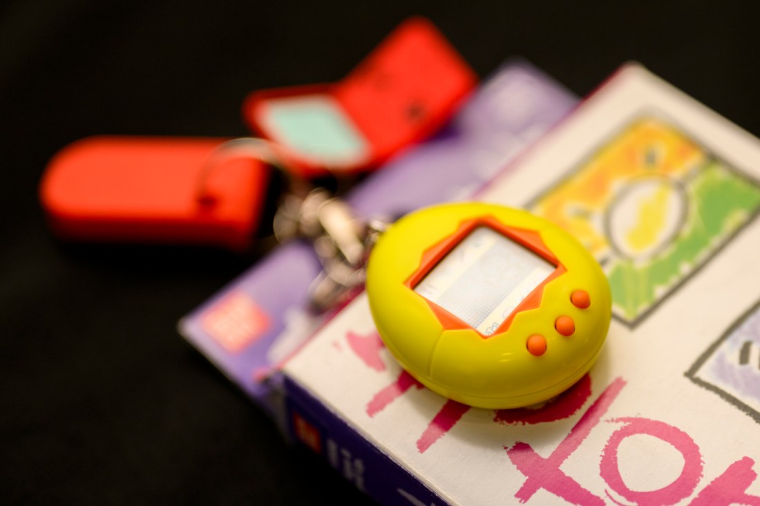 An egg-shaped Tamagotchi device with a rectangular screen and three small buttons at the bottom. 