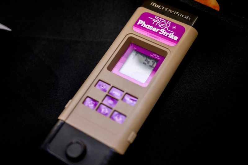 A rectangular gaming device with a small screen and several purple buttons that says 'Star Trek Phaser Strike' on it.