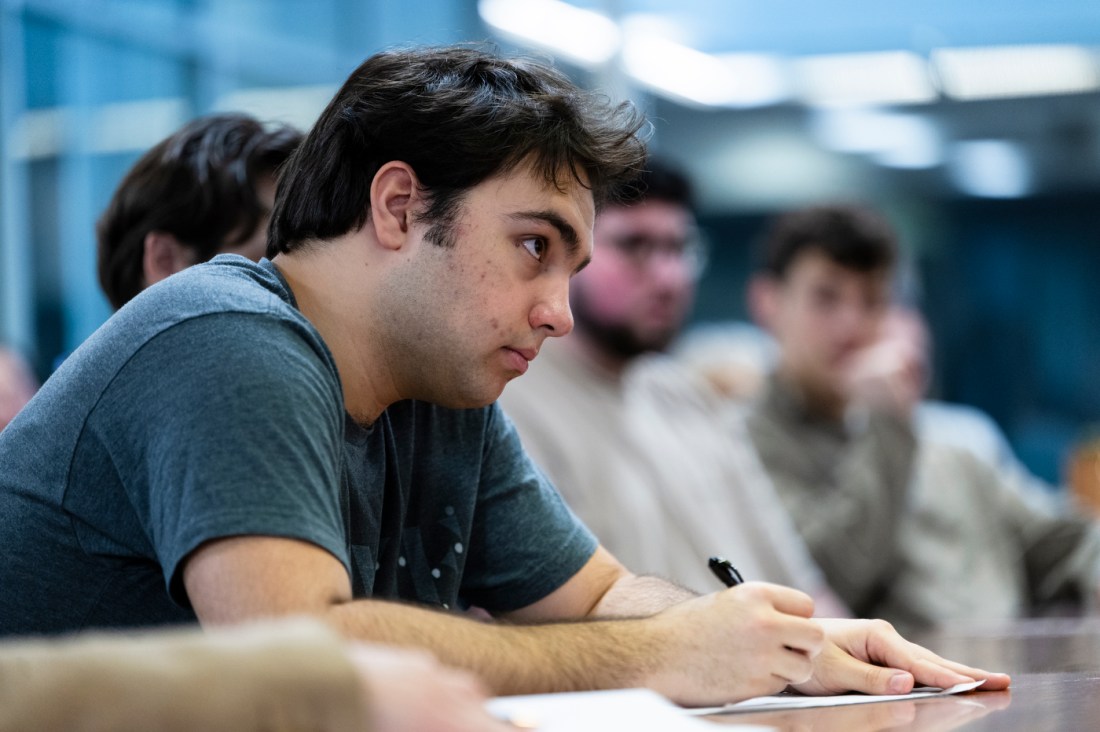 An audience member taking notes with pen on paper at a lecture.