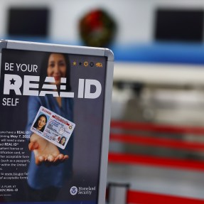 A sign in an airport that says 'Real ID' on it with a person holding a drivers license card.