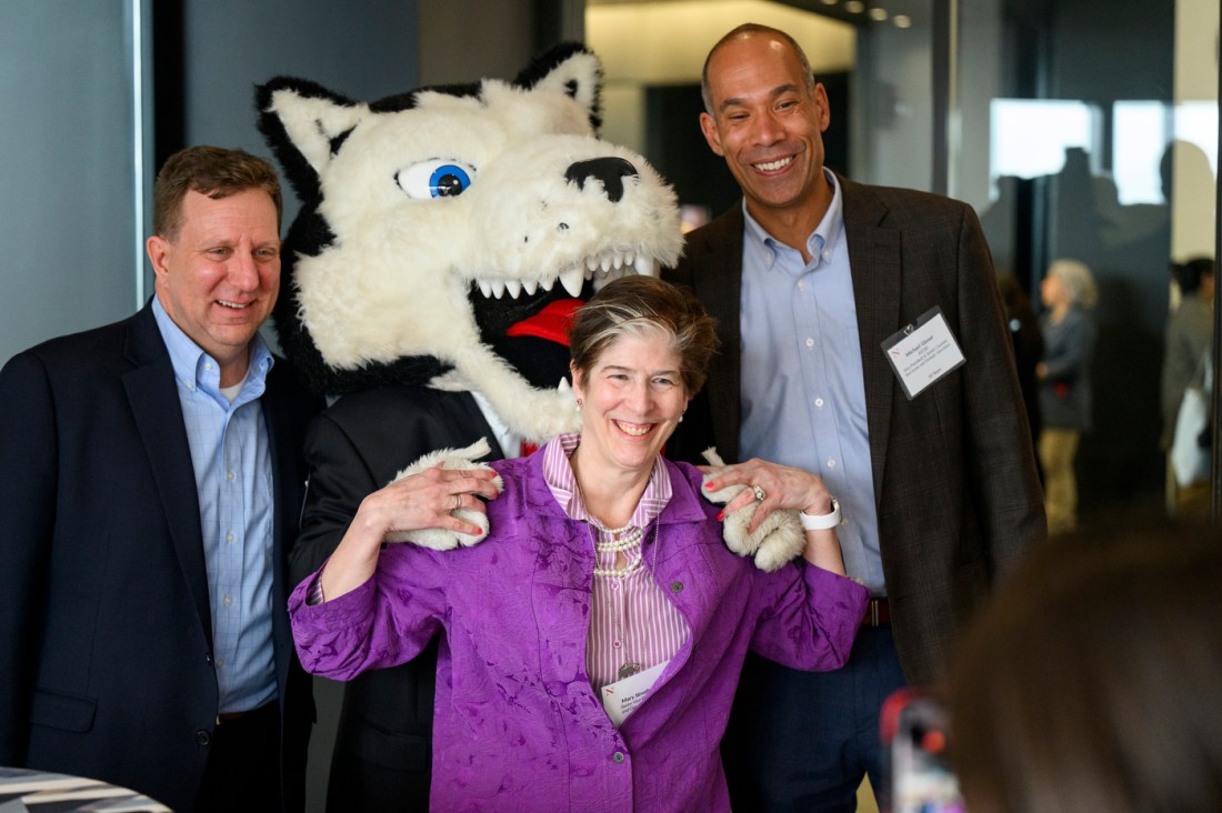 Three people posing with Paws, the husky mascot. 