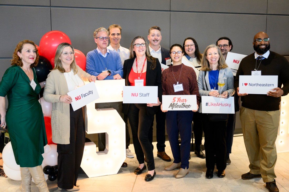 A group of Northeastern community members posing with signs that say '5 Year Milestone'. 