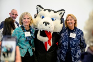 Two members of the Northeastern community posing with Paws, the Husky mascot.