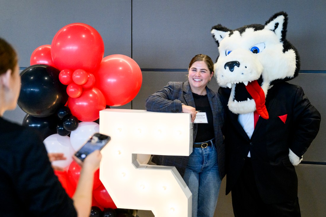 Fernanda Hurtado Ortiz, a Northeastern staff member, posing with Paws, the Husky mascot in front of a large number 5 prop next to a balloon arch.