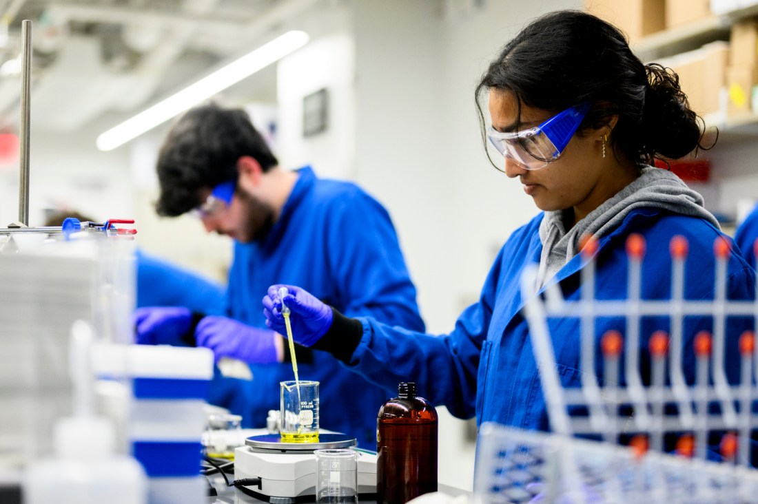 Several students with lab coats and goggles creating cosmetics in a lab.