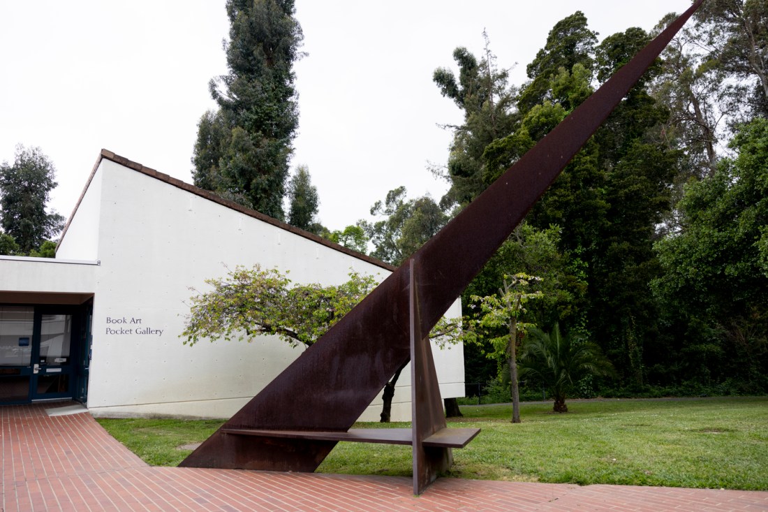 A large sundial outside on a green lawn next to a pathway in front of a building that says 'Book Art Pocket Gallery' on it.