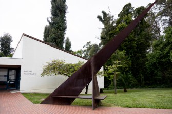 A large sundial outside on a green lawn next to a pathway in front of a building that says 'Book Art Pocket Gallery' on it.
