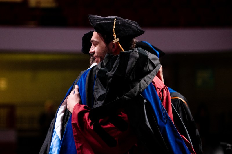 Two people hugging on stage at the PhD Hooding and Commencement.