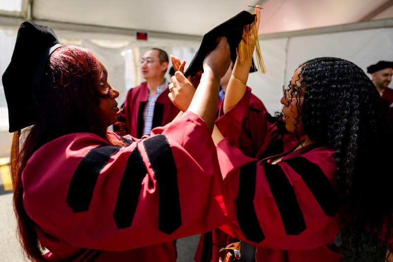 A PhD grad helps another grad adjust their grad cap.