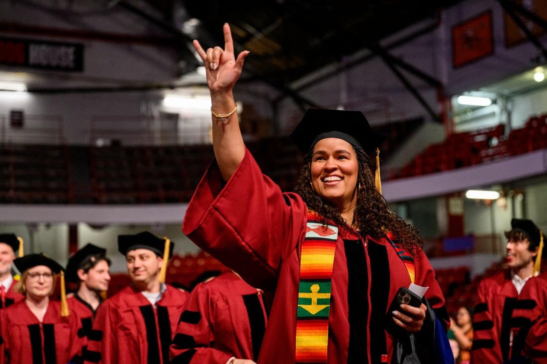 A graduate raising their hand in the air at the PhD Hooding and Ceremony.
