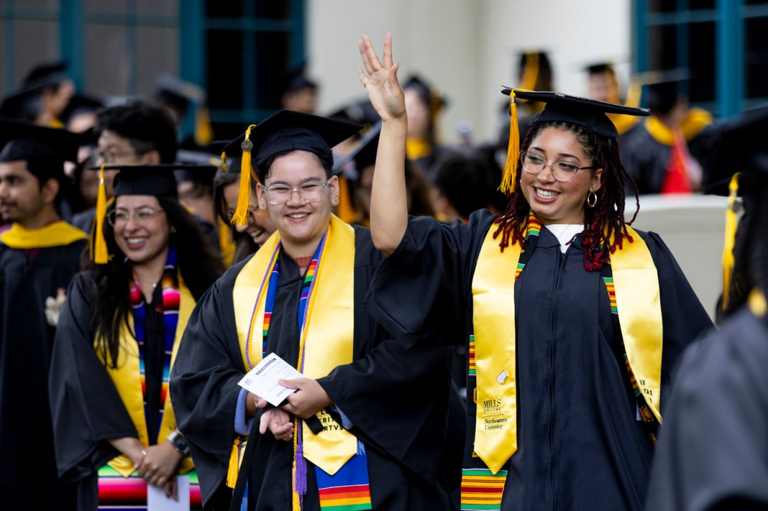 A graduate holding up a hand signal and smiling at the Oakland commencement ceremony.