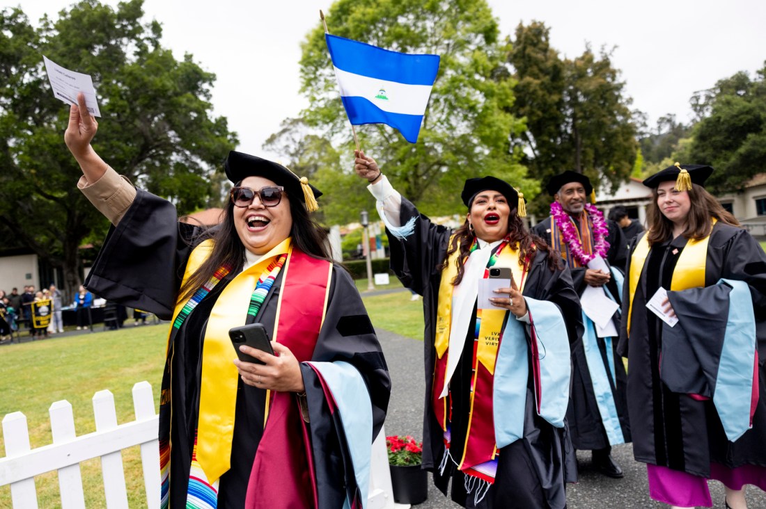 Graduates waving flags and pieces of paper while smiling and walking outside.