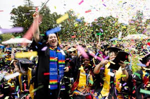 A graduate waving and cheering as confetti falls around them at the Oakland Commencement ceremony.