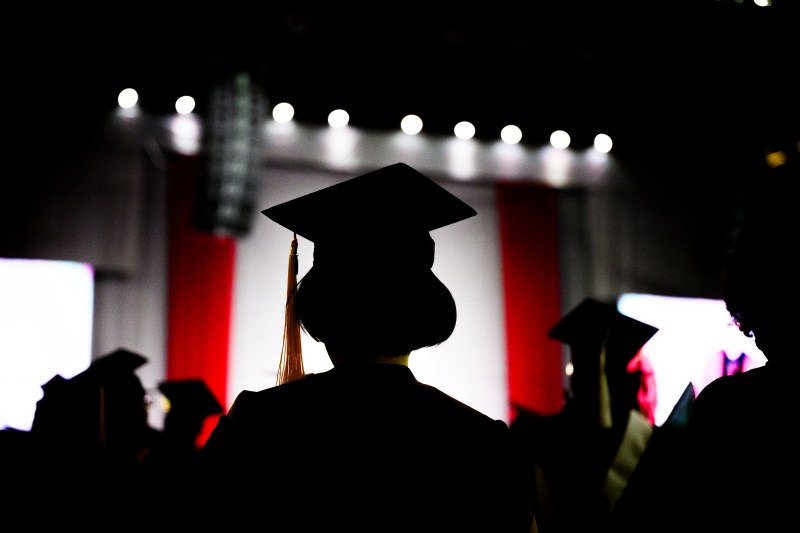 A silhouette of a graduate wearing a cap and gown in Matthews Arena.