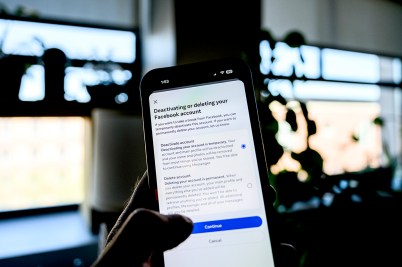 A person's hand holding up an iPhone ready to press the 'deactivate' button on Facebook with their thumb.