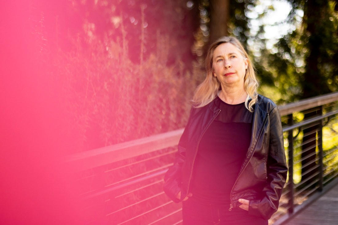 Portrait of Juliana Spahr, standing outside wearing black in front of greenery