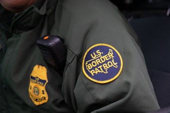 A border patrol agent's jacket with a 'US Border Patrol' patch on the sleeve and a radio on the front.