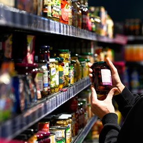 A person holding a jar of olives off of the shelf at a grocery store.