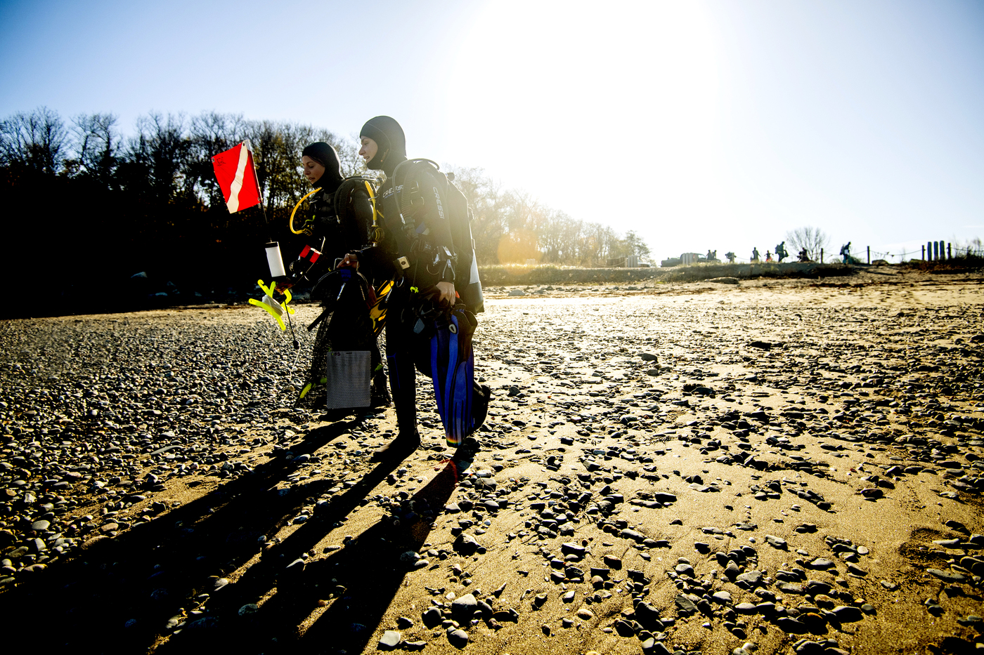 Two students walking across the beach in Nahant wearing diving gear.