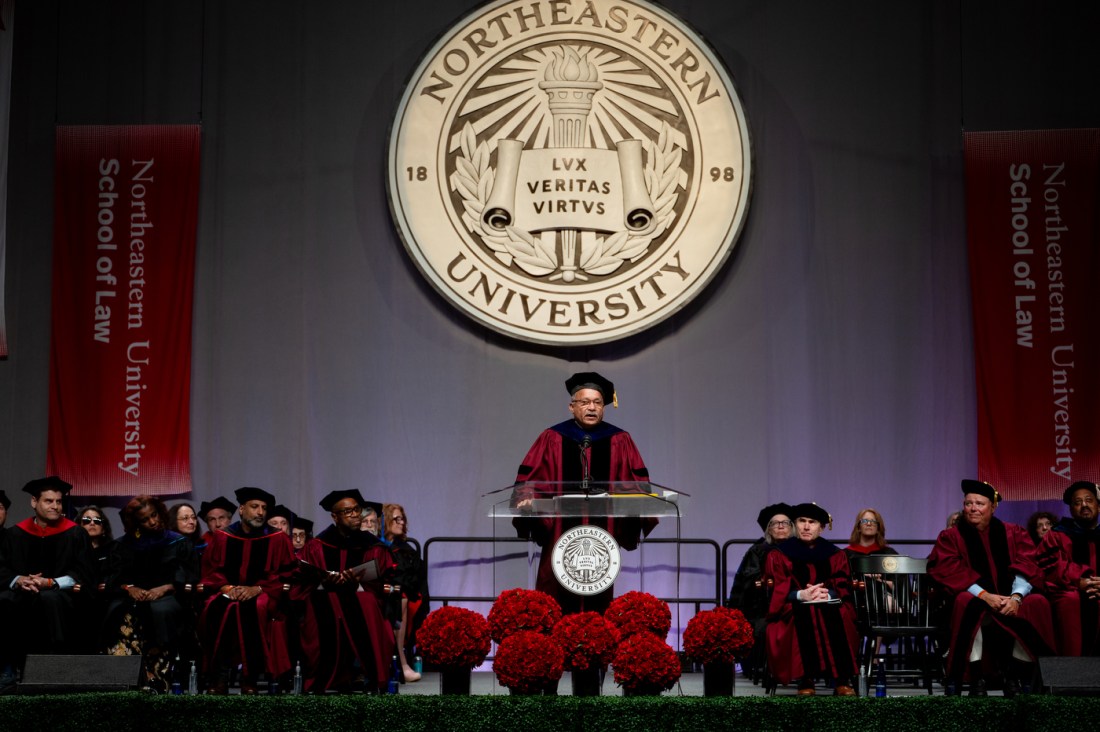 Ralph Martin standing on stage at Matthews Arena speaking into a microphone at a podium.