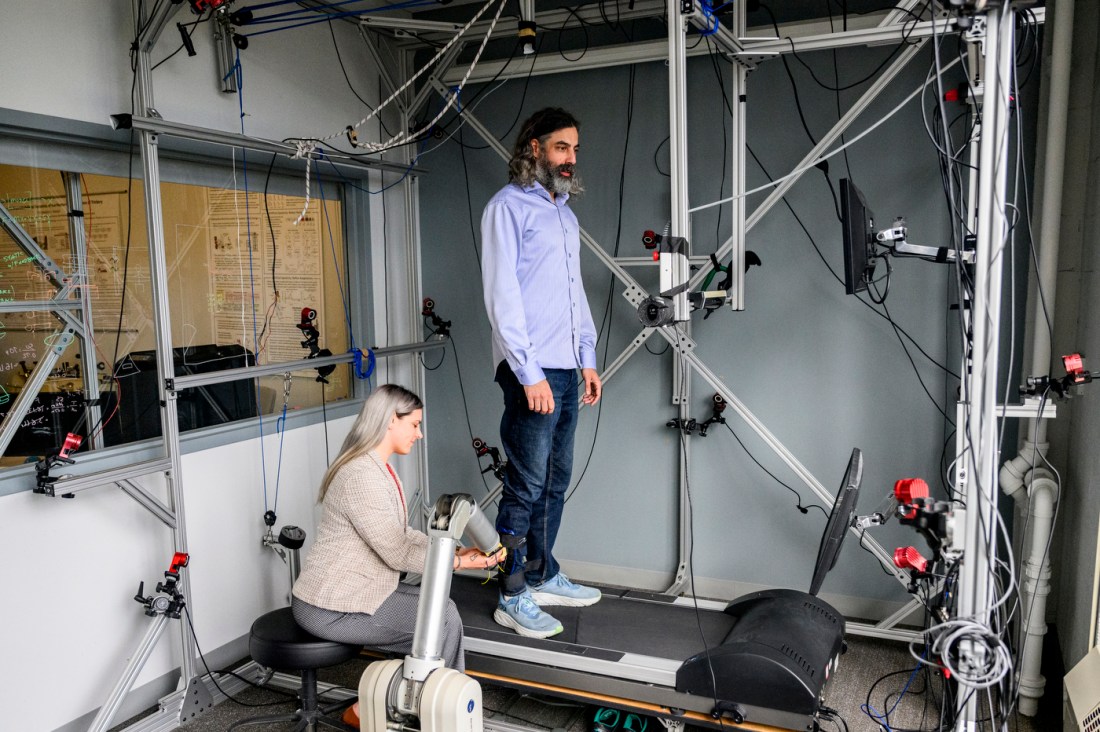 Julia Manczurowsky observes a subject walking in a biomechanics lab with metal scaffolding and cables connected to sensors.