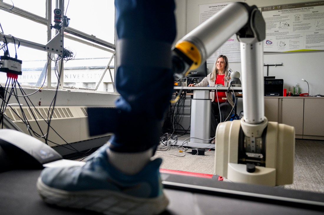 A person's foot in a motion capture lab with sensors wrapped around it as the person it belongs to walks on a treadmill surrounded by research equipment.