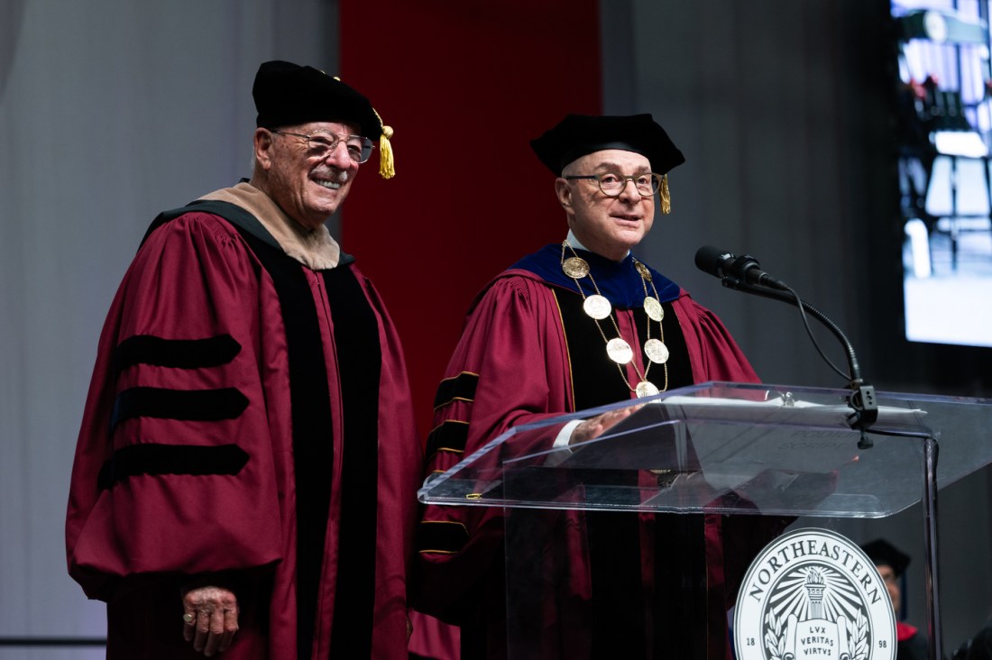 Northeastern President Joseph E. Aoun and a speaker stand at the podium during the Pioneer Award presentation at the D’Amore-McKim School of Business Undergraduate Commencement.