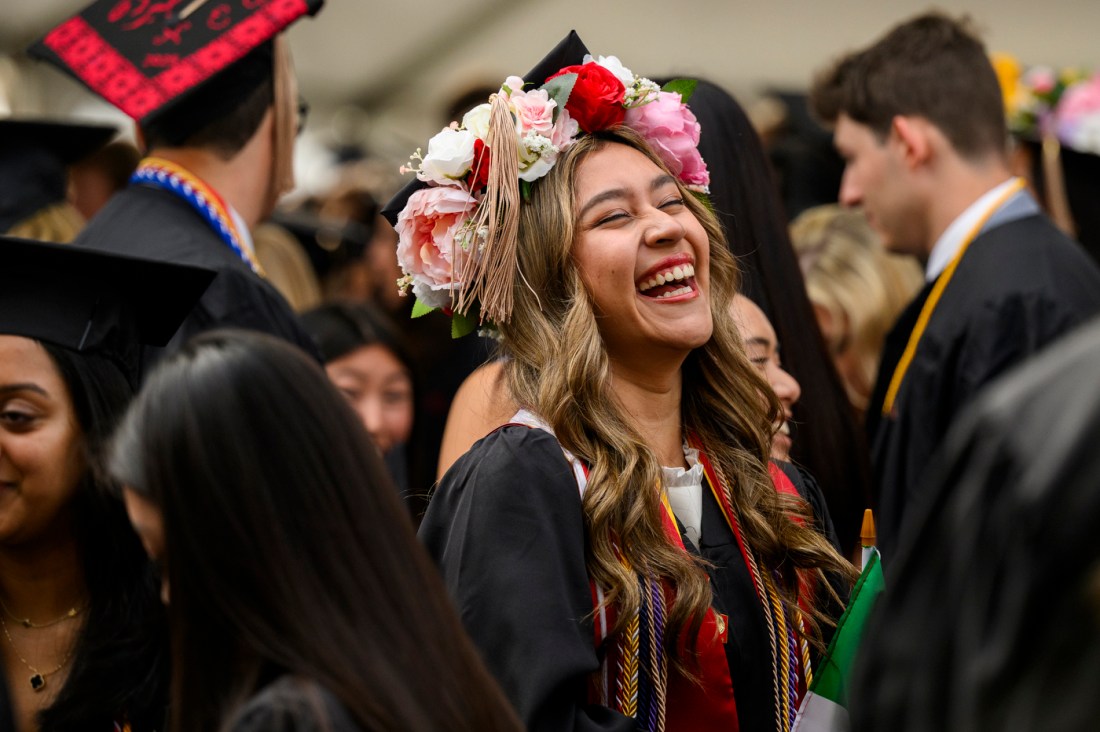 A smiling graduate wearing a floral crown among a group of students in academic regalia.
