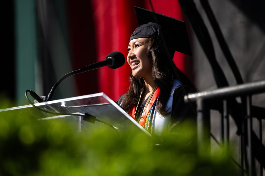 Graduate poses in cap and gown while smiling and walking across the Commencement stage.
