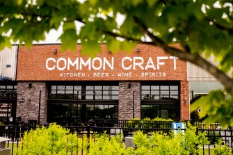A tree in the foreground of a shot of a brick building that says 'Common Craft' on it in all white, all caps letters.