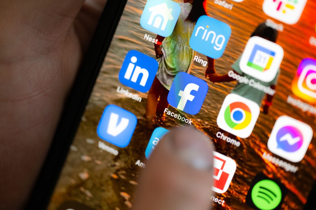 A person's thumb hovers over the Facebook icon on a smartphone.