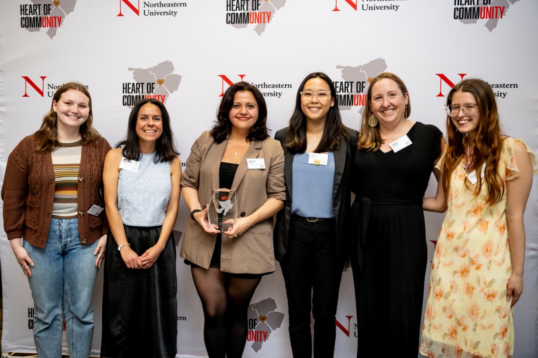 A group photo of six women posing together in front of a step-and-repeat backdrop featuring "HEART OF COMMUNITY" and Northeastern University logos.