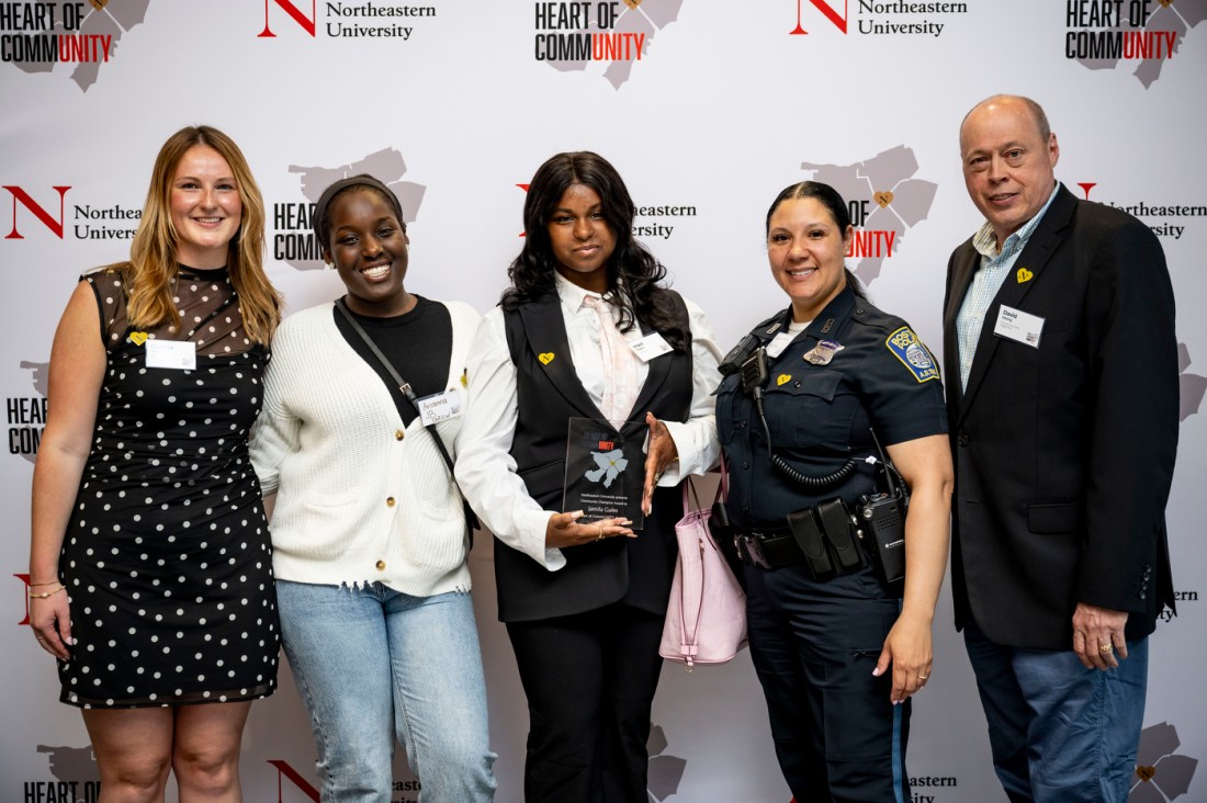 A smaller group photo of six people, including what appears to be a uniformed police officer on the right, posed together in front of the branded backdrop. The group consists of individuals in professional attire, smiling at the camera.