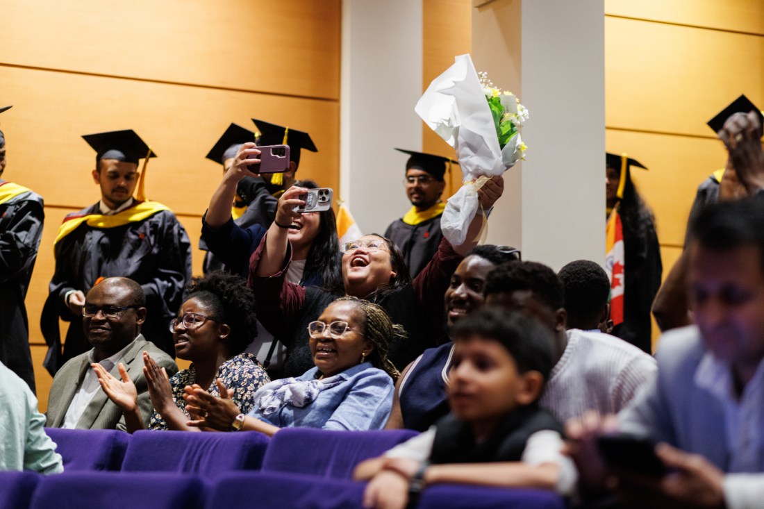 A crowd of happy graduates and family members celebrate, with some taking photos and holding flowers, showing diverse faces filled with joy and accomplishment.